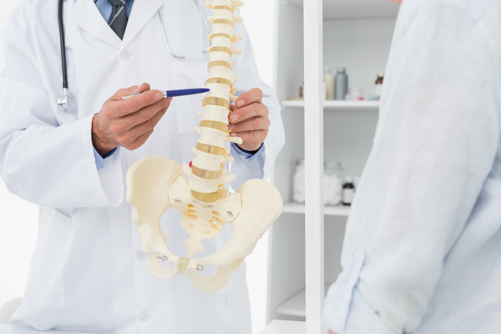 Especialista en columna vertebral señalando con un bolígrafo un modelo de columna vertebral para explicar problemas estructurales o nerviosos.
