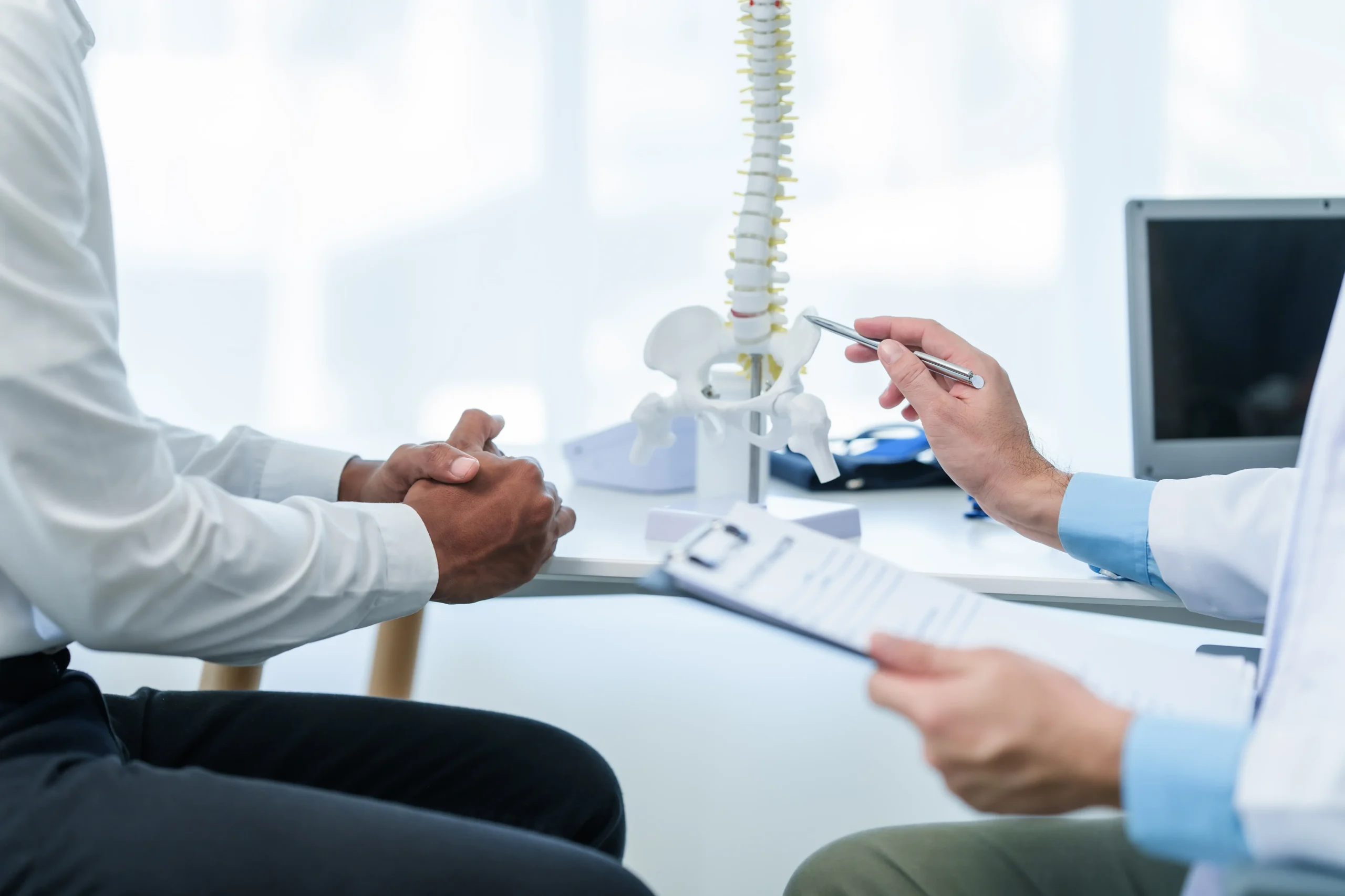 Un médico muestra un modelo de columna vertebral a un paciente mientras le explica las causas del dolor musculoesquelético y las opciones de tratamiento en una consulta médica.